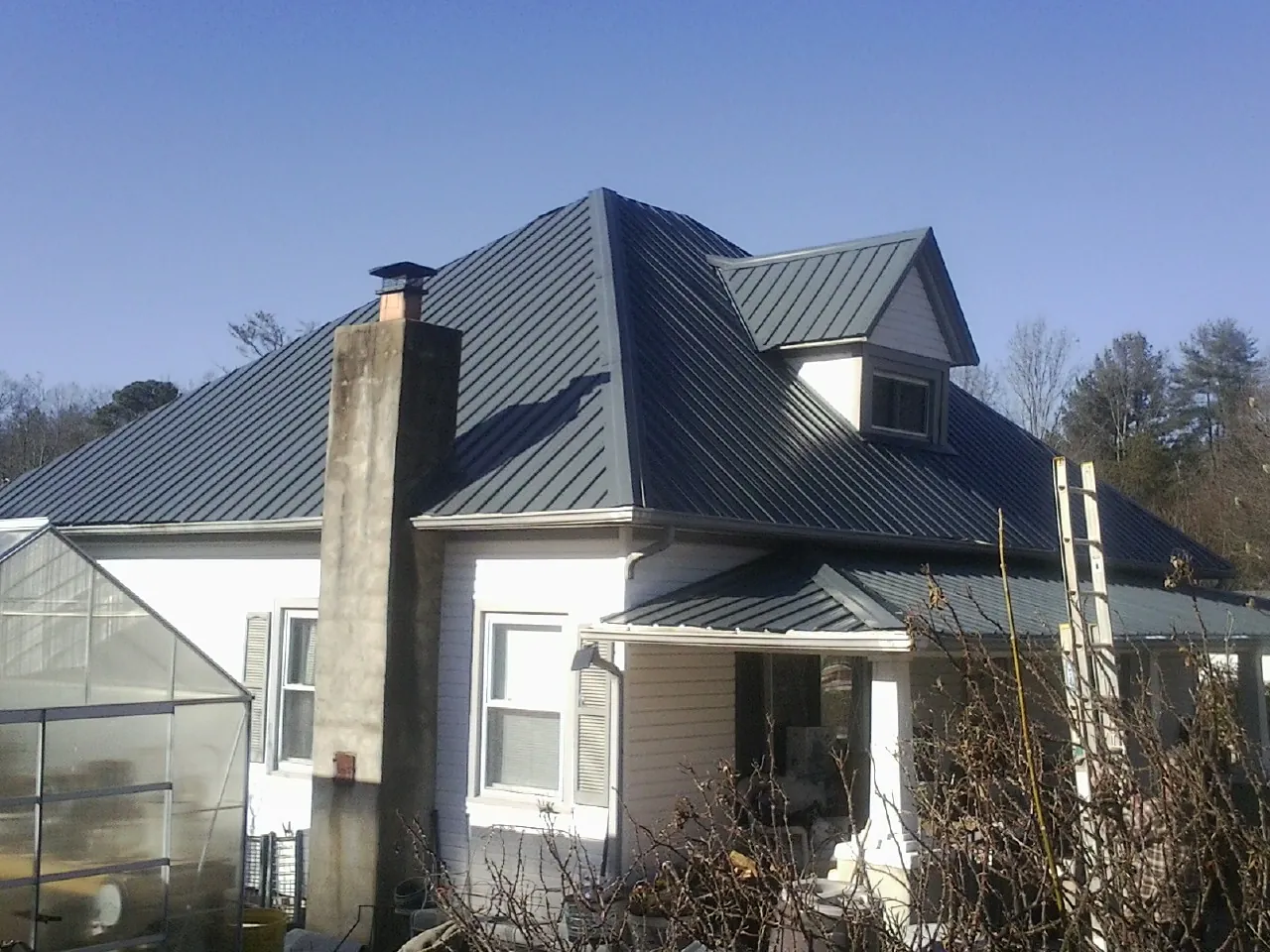 Dark blue standing seam metal roof on a white farmhouse with dormer — Slate & Tile Roof Repair by Roofing Brothers in Exeter