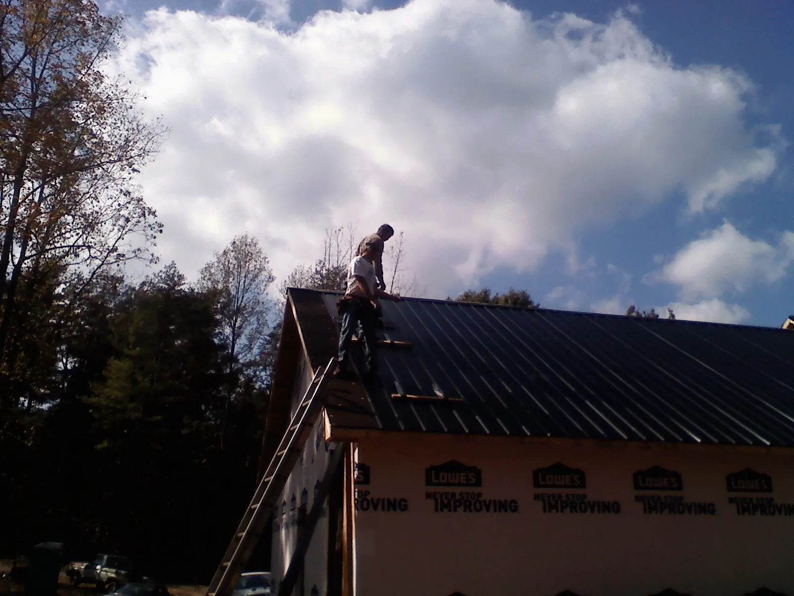 Roofer fastening dark metal panels high against a cloudy sky, from a Roof Inspection job in Exeter